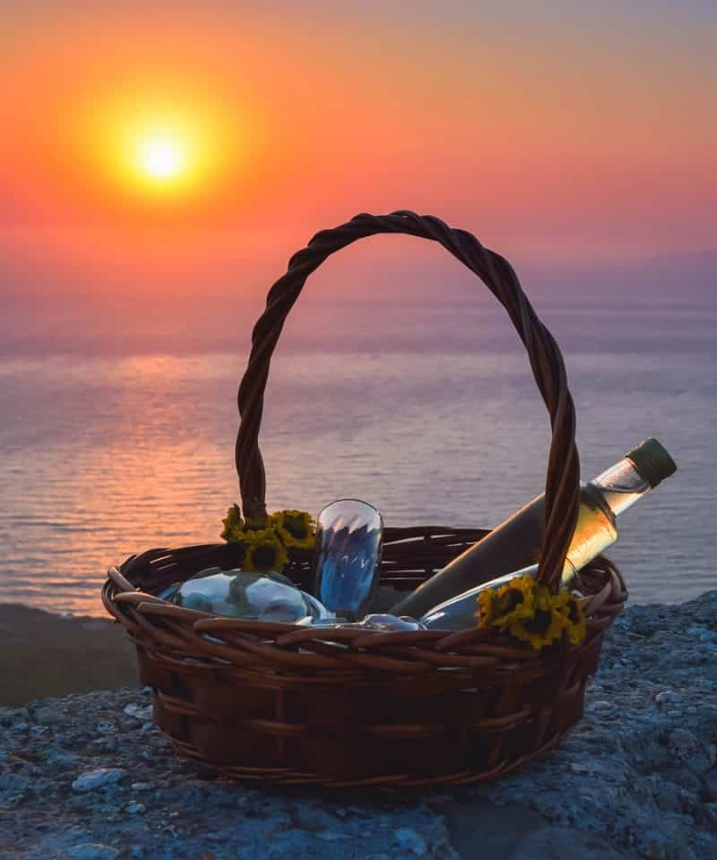 Picnic basket with wine and glasses at sunset by the sea